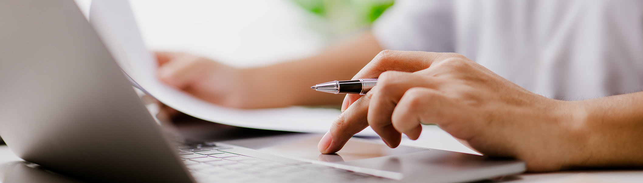 Hand hält einen Stift über einer Laptop-Tastatur auf einem reflektierenden Tisch